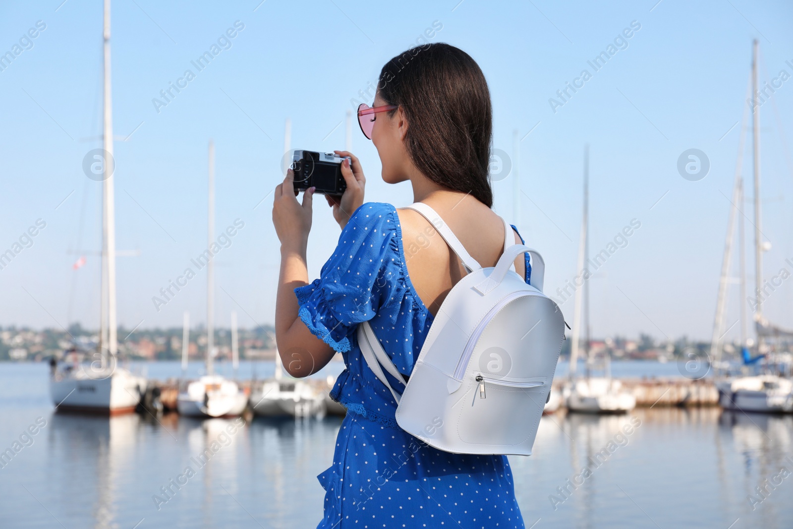Photo of Young woman with stylish backpack and camera near river on sunny day, back view