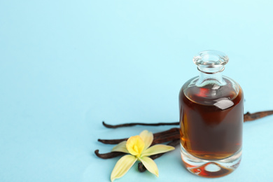 Photo of Aromatic homemade vanilla extract on light blue background. Space for text