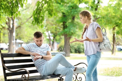 Photo of Young couple arguing while sitting on bench in park. Problems in relationship