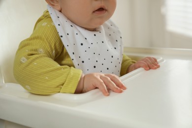 Photo of Cute little baby wearing bib in highchair indoors, closeup