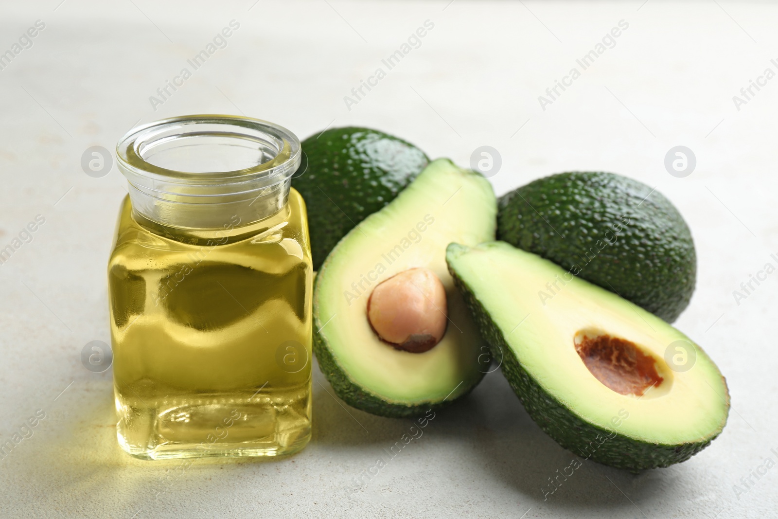 Photo of Jar of natural oil and avocados on grey stone background