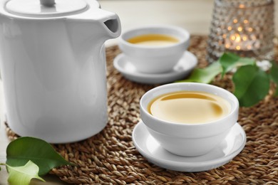 Photo of Green tea in white cups with leaves and teapot on table, closeup