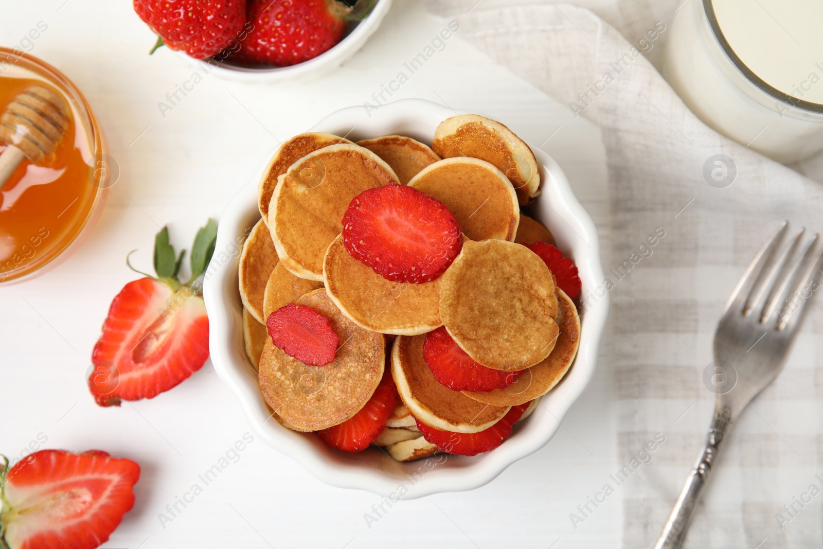 Photo of Delicious mini pancakes cereal with strawberries served on white wooden table, flat lay