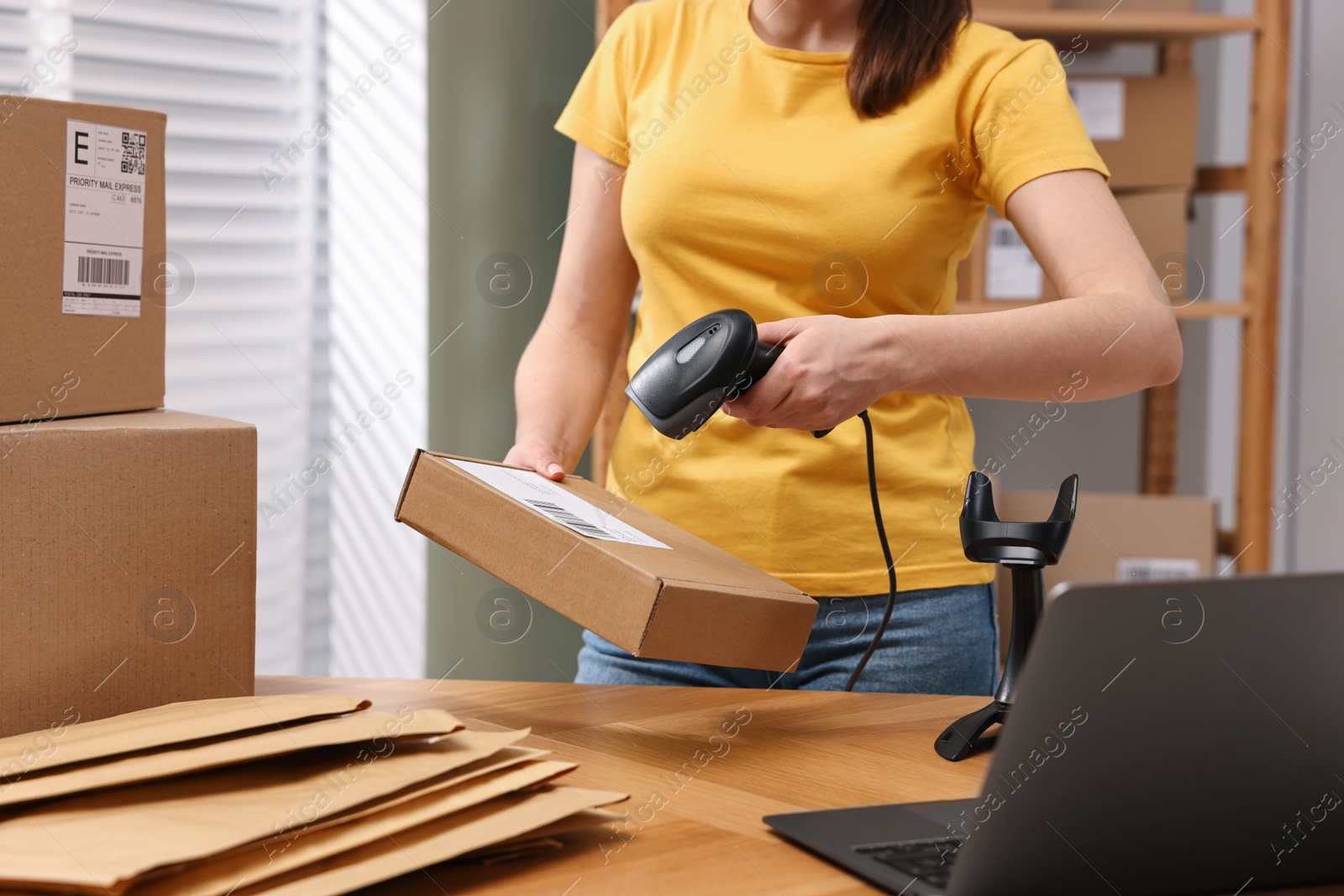 Photo of Parcel packing. Post office worker with scanner reading barcode at wooden table indoors, closeup