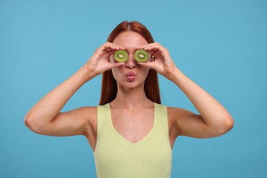 Photo of Funny woman covering eyes with halves of fresh kiwi on light blue background
