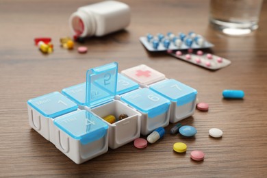 Plastic box with different pills on wooden table