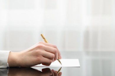Photo of Woman writing on sheet of paper at glass table, closeup