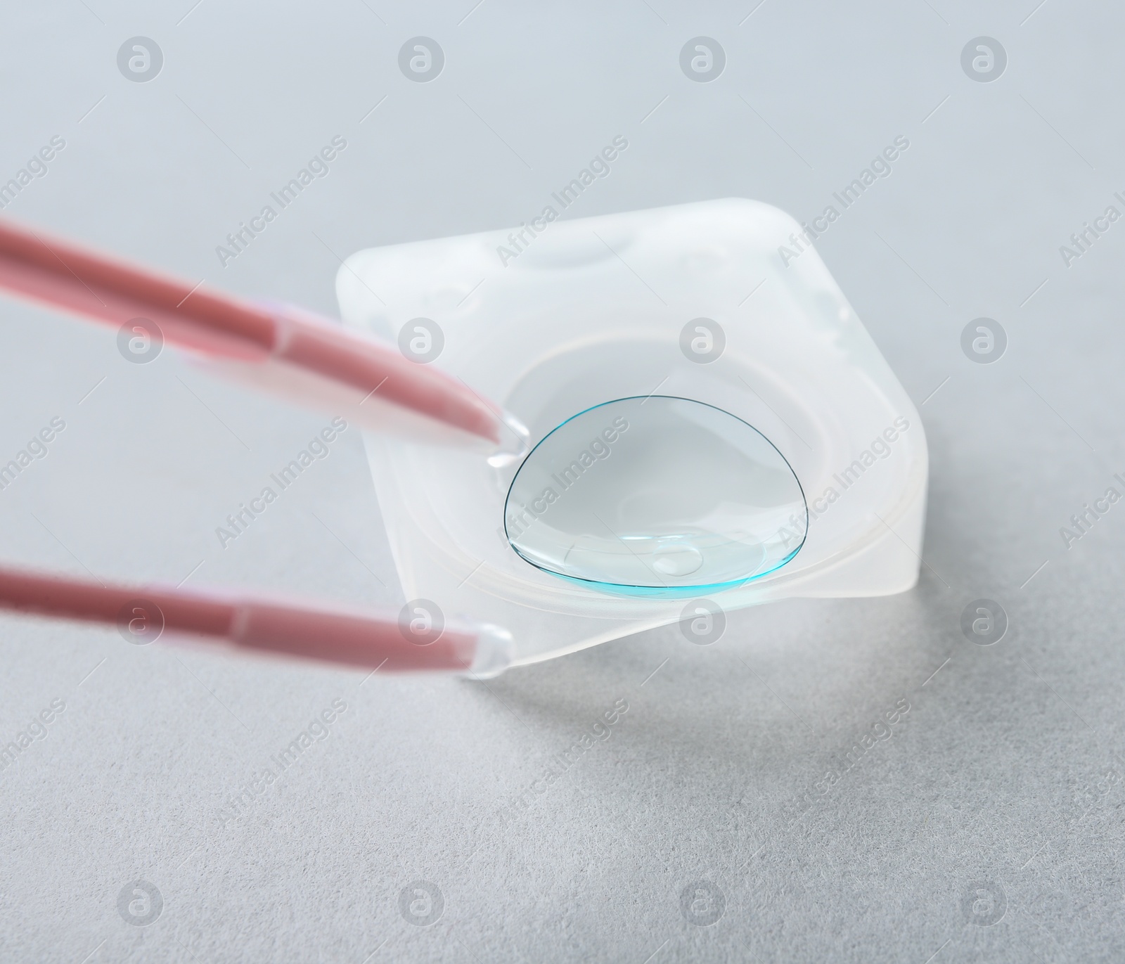 Photo of Tweezers with contact lens on light background, closeup