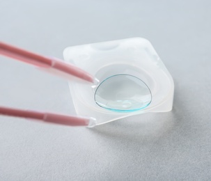 Photo of Tweezers with contact lens on light background, closeup