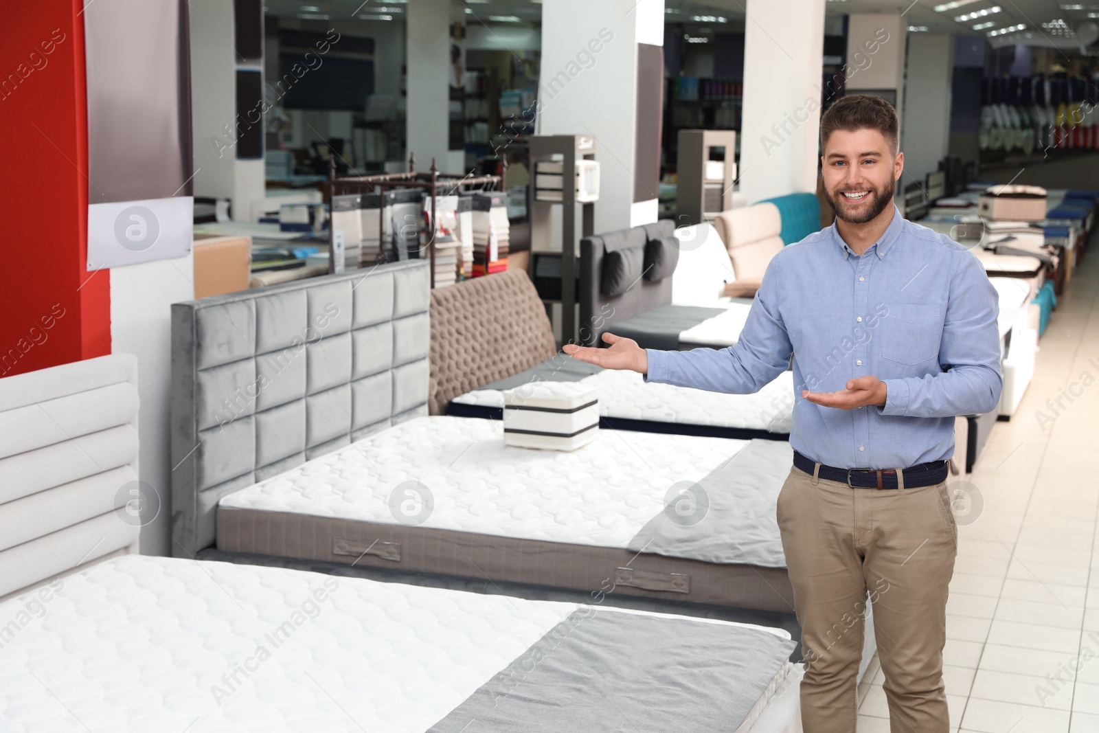 Photo of Young salesman showing modern orthopedic mattress in store