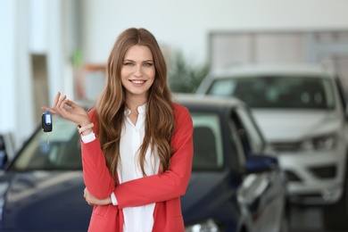 Photo of Attractive young saleswoman holding key in car dealership