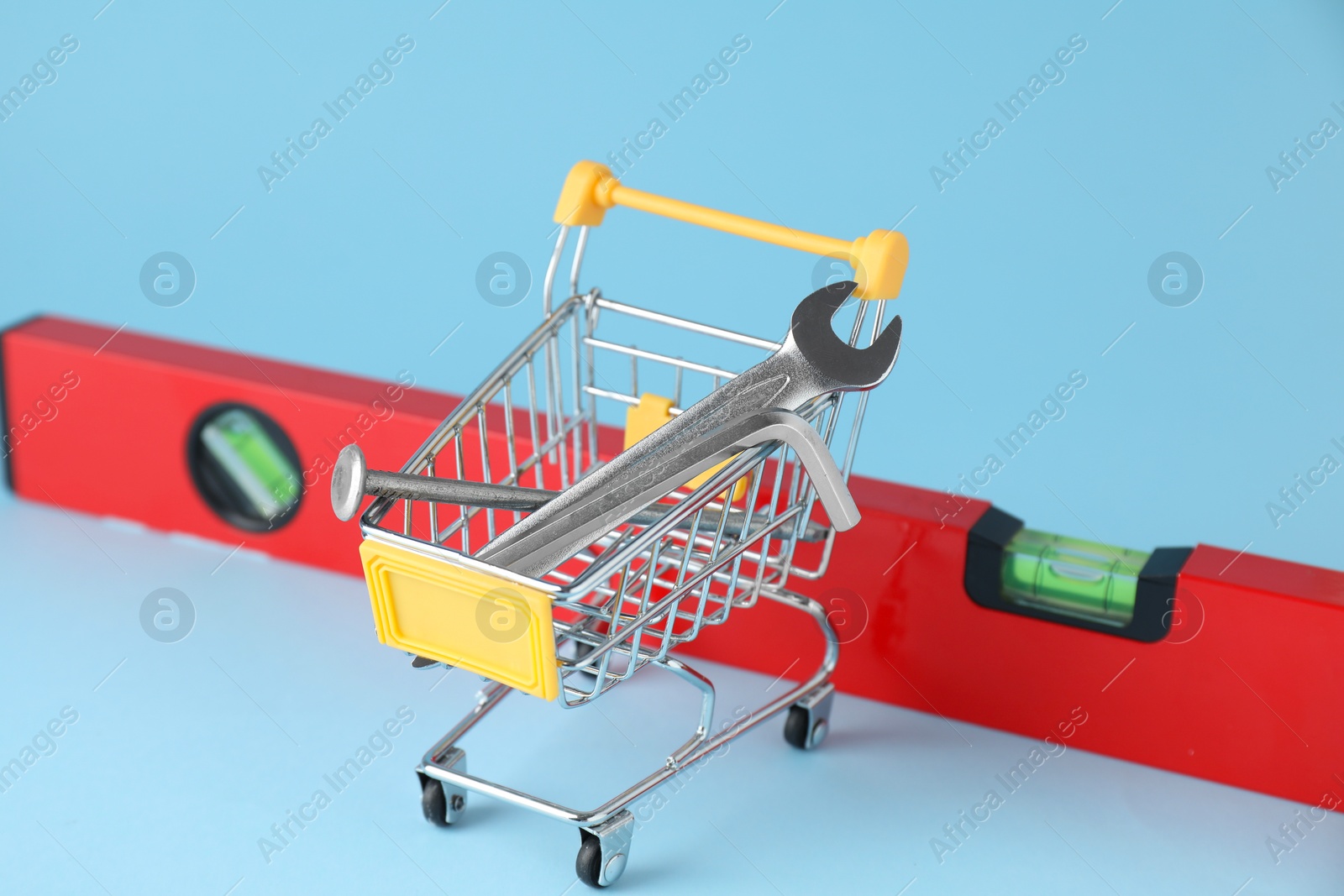 Photo of Shopping cart with different construction tools on light blue background