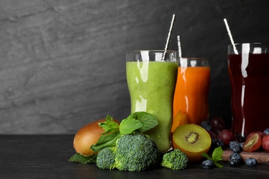 Photo of Delicious colorful juices in glasses and fresh ingredients on black table. Space for text