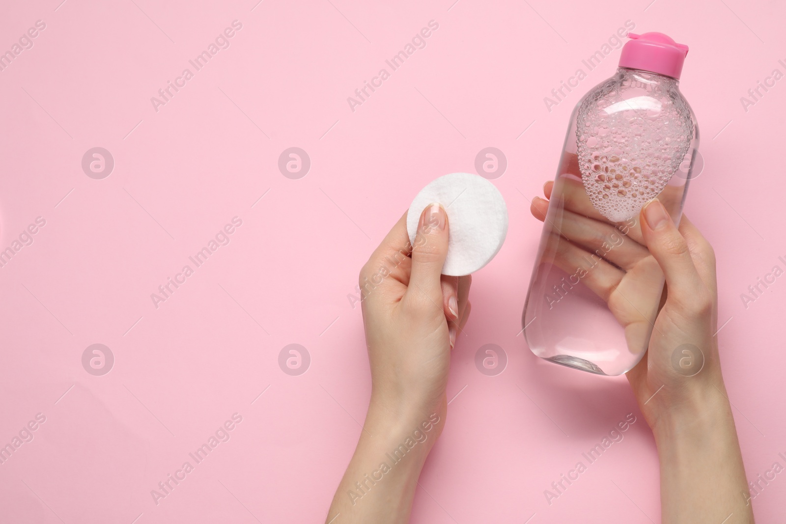 Photo of Woman holding makeup remover and cotton pad on pink background, top view. Space for text