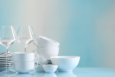 Photo of Set of many clean dishware and glasses on light blue table. Space for text