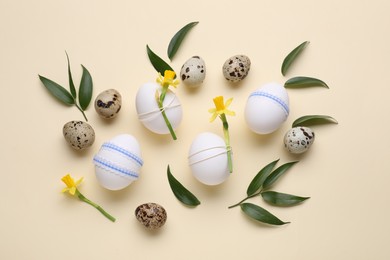 Festively decorated Easter eggs, green leaves and flowers on beige background, flat lay