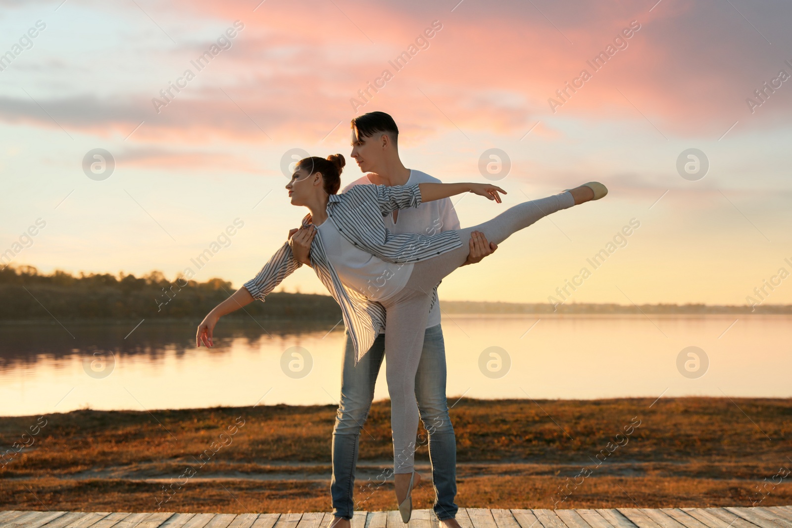 Photo of Beautiful young couple practicing dance moves near river at sunset