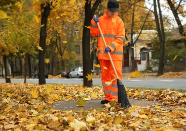 Street cleaner sweeping fallen leaves outdoors on autumn day