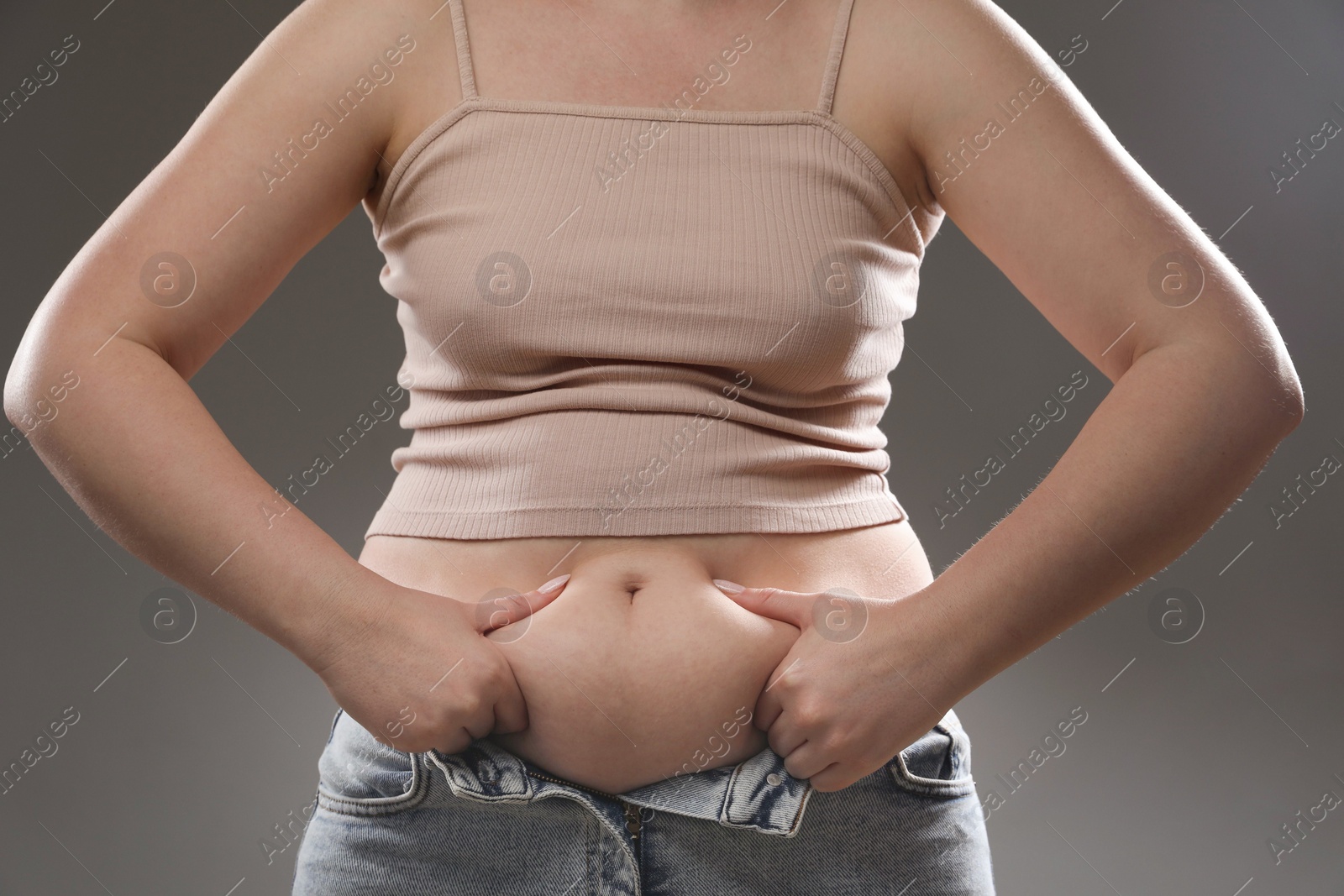 Photo of Woman touching belly fat on grey background, closeup. Overweight problem