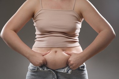 Woman touching belly fat on grey background, closeup. Overweight problem