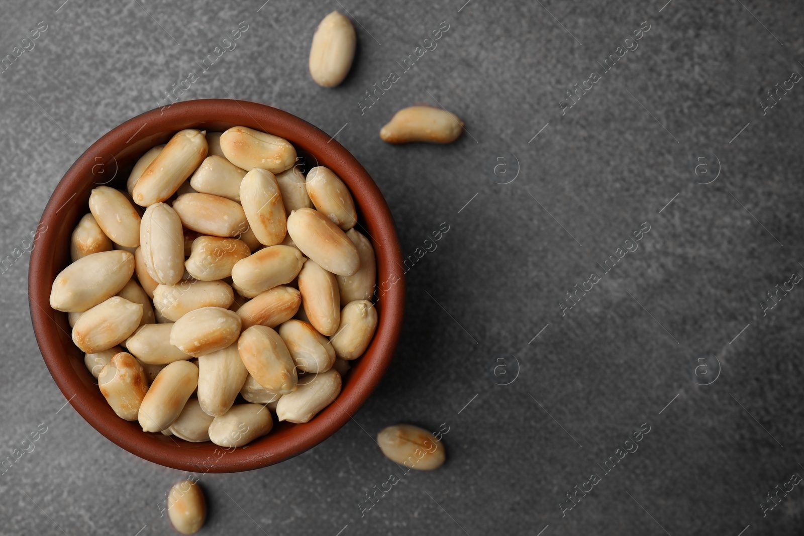 Photo of Roasted peanuts in bowl on brown table, top view. Space for text