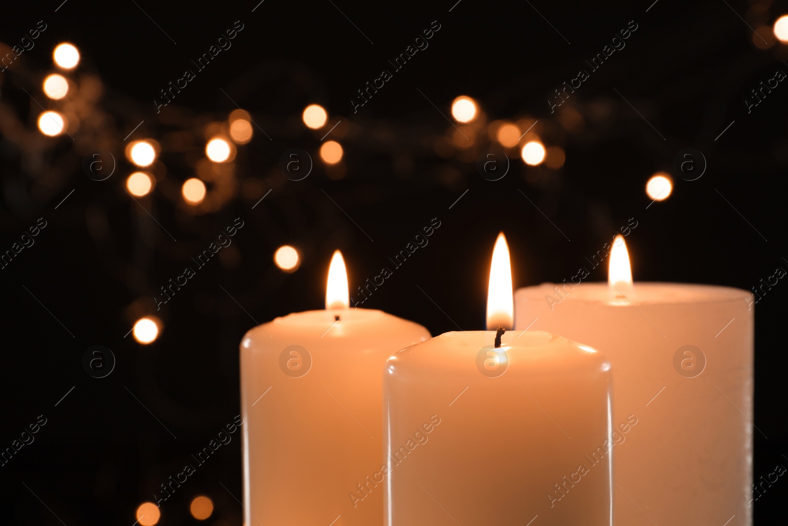 Photo of Wax candles burning against blurred lights in darkness