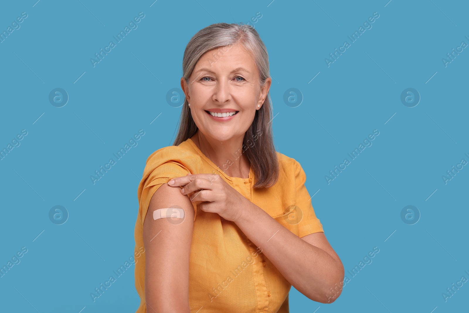 Photo of Senior woman with adhesive bandage on her arm after vaccination against light blue background