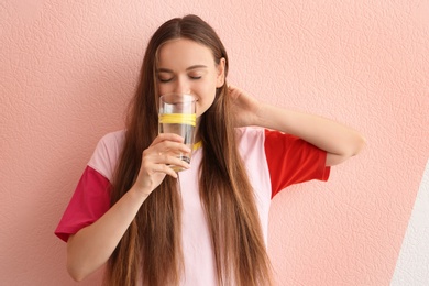 Young woman drinking lemon water on color background