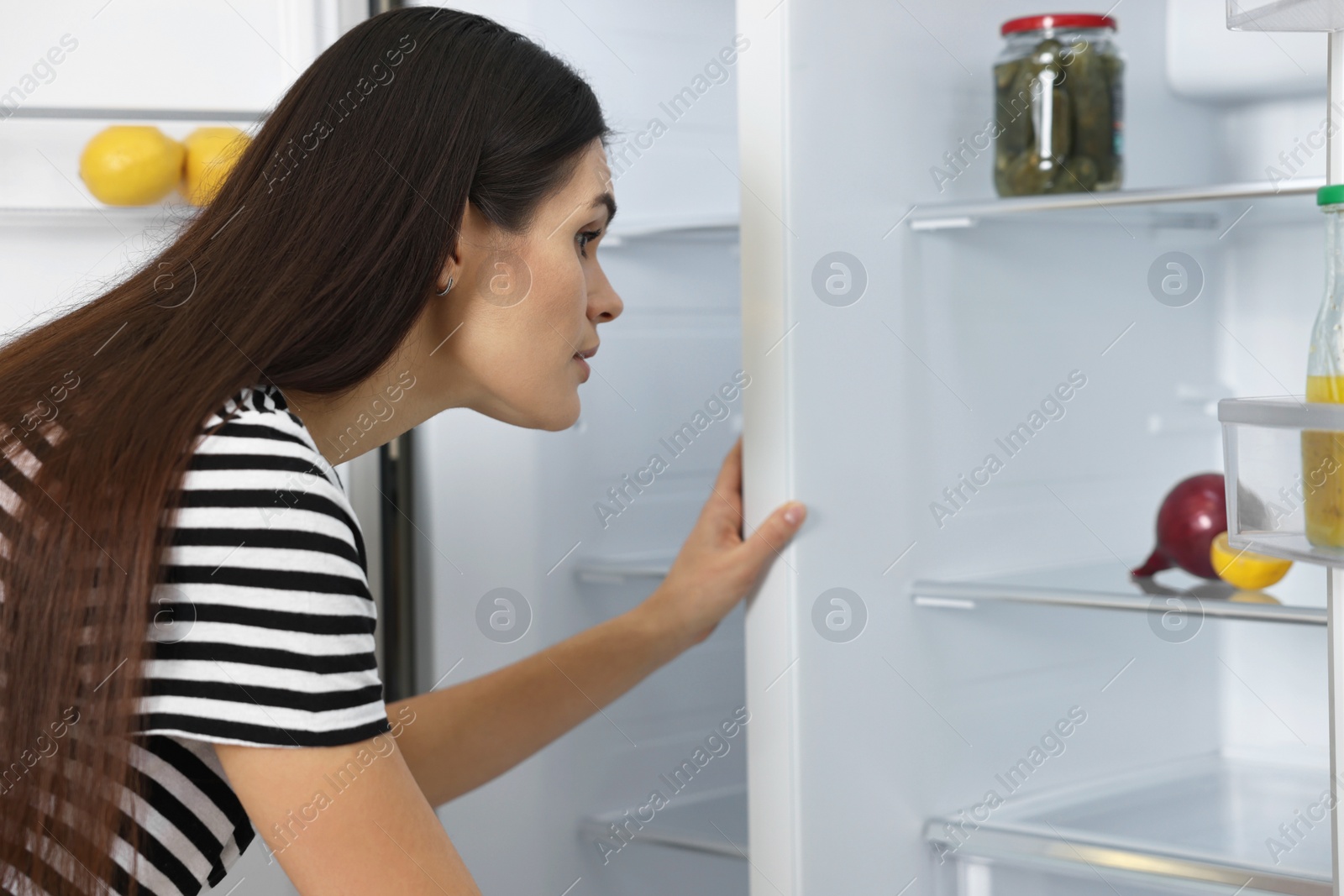 Photo of Upset young woman looking into empty refrigerator