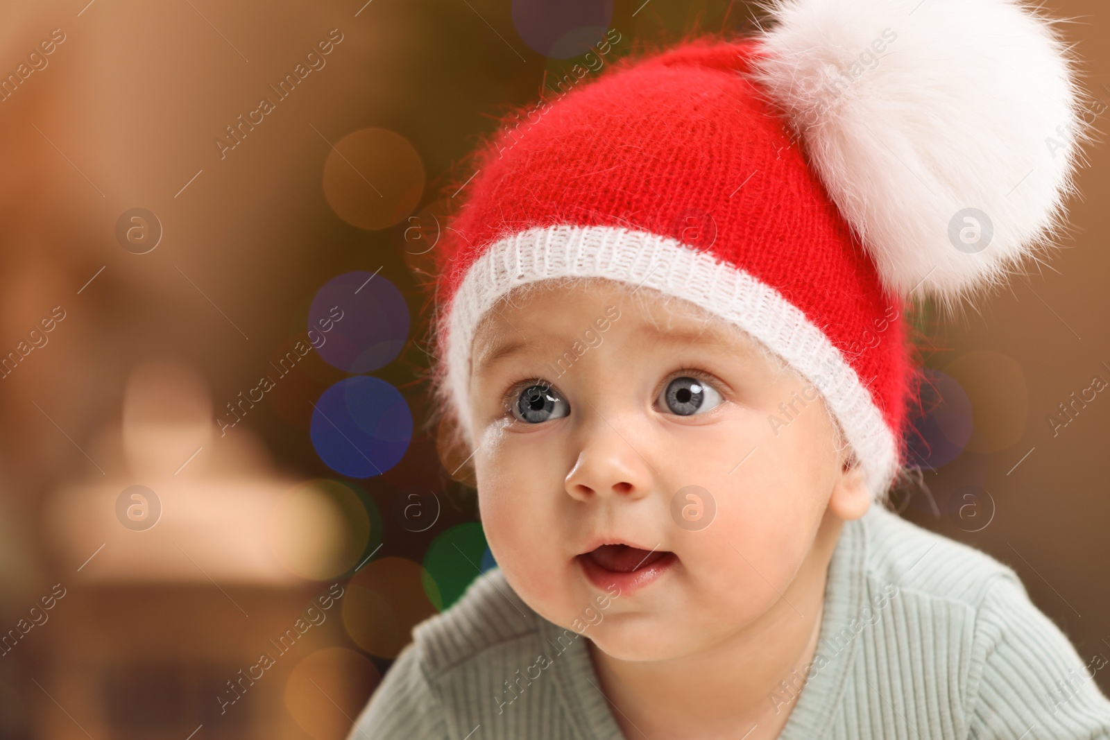 Photo of Cute little baby and blurred Christmas lights on background, space for text. Winter holiday