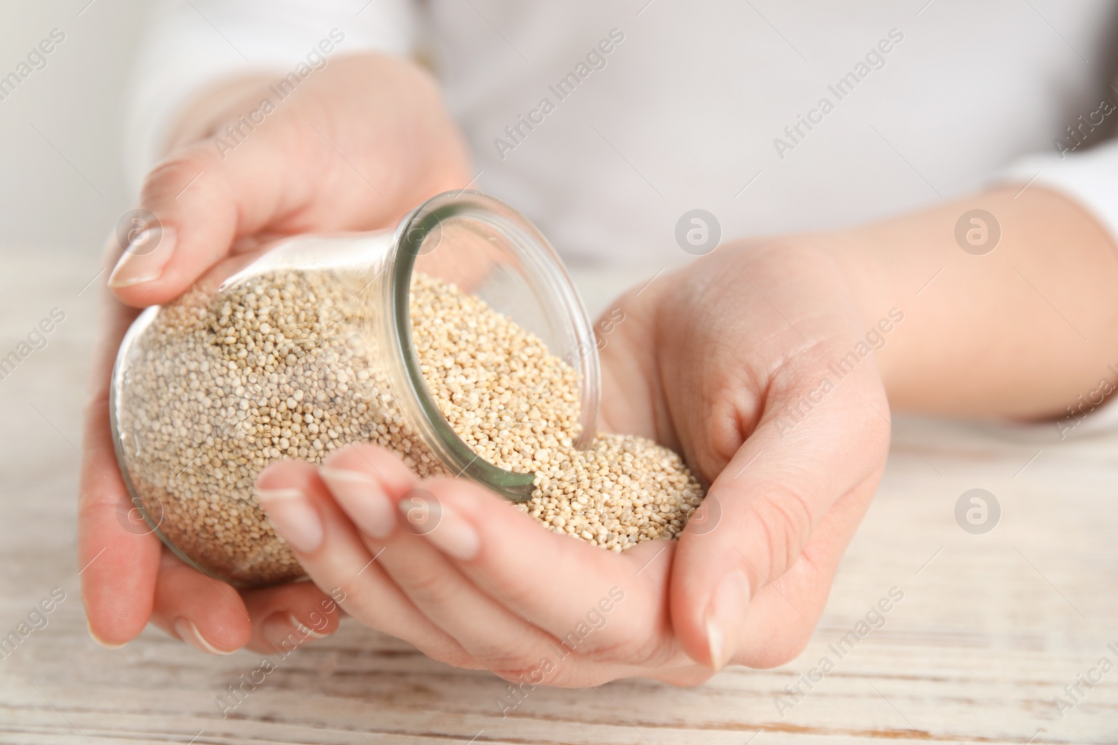 Photo of Woman with jar of white quinoa at wooden table, closeup