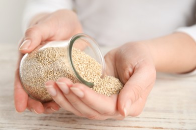 Photo of Woman with jar of white quinoa at wooden table, closeup