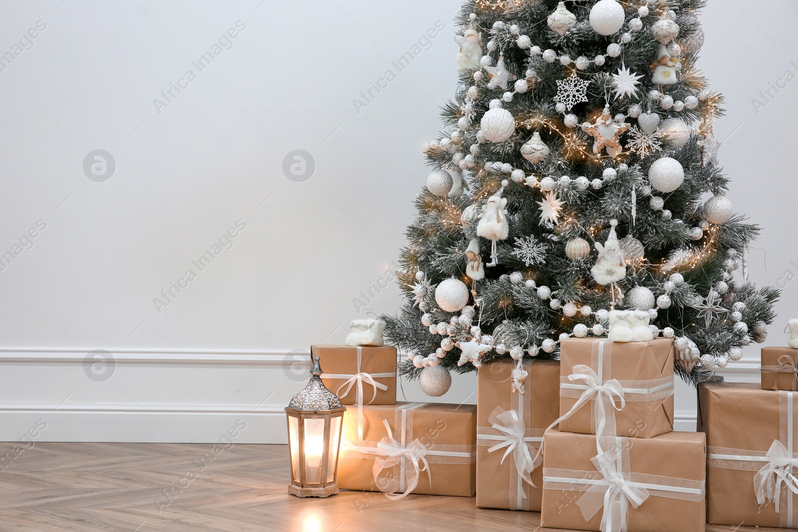 Photo of Beautiful decorated Christmas tree and gifts near light wall. Space for text