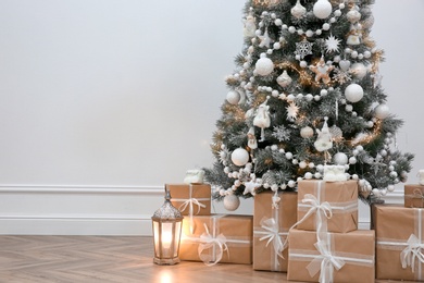 Photo of Beautiful decorated Christmas tree and gifts near light wall. Space for text