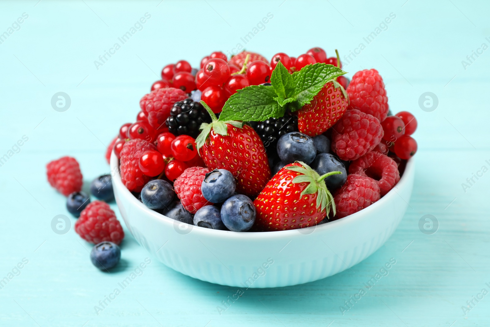 Photo of Mix of different fresh berries and mint in bowl on light blue wooden table