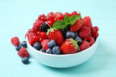 Photo of Mix of different fresh berries and mint in bowl on light blue wooden table