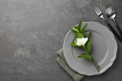 Photo of Stylish setting with cutlery, napkin, flower and plate on grey textured table, flat lay. Space for text