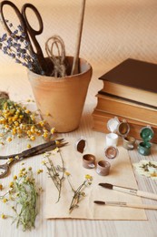 Photo of Beautiful dried flowers, books, brushes and paints on wooden table
