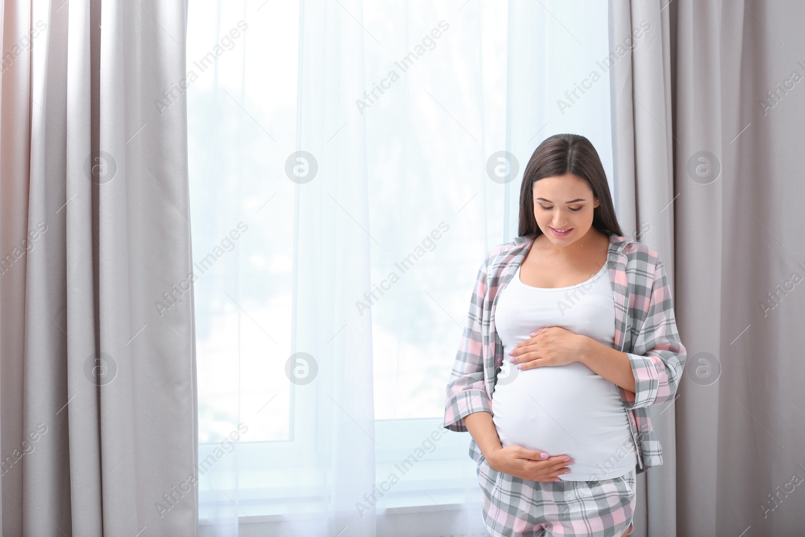 Photo of Young beautiful pregnant woman near window at home