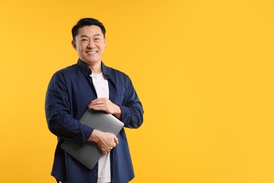 Photo of Portrait of happy man with laptop on yellow background. Space for text