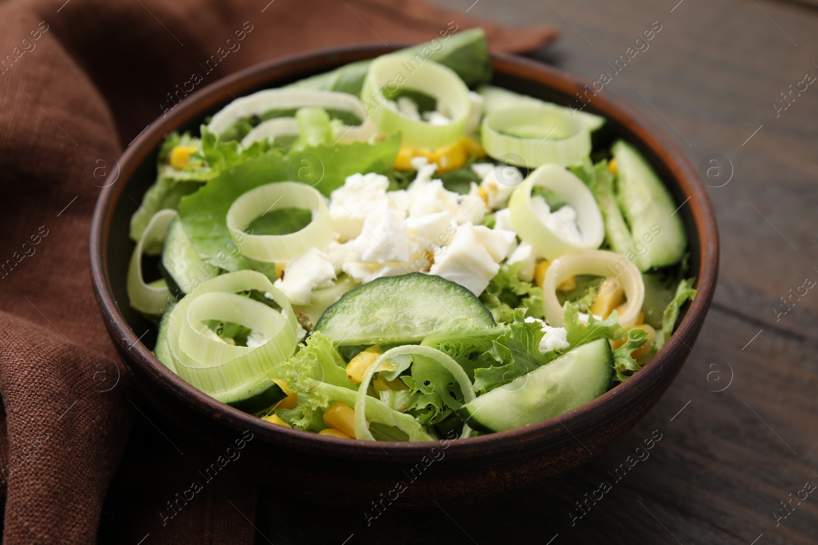 Photo of Bowl of tasty salad with leek and cheese on wooden table, closeup