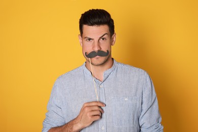 Funny man with fake mustache on yellow background