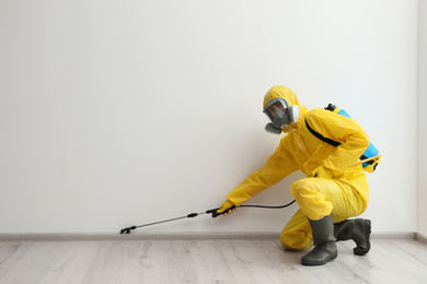 Pest control worker in protective suit spraying pesticide indoors. Space for text