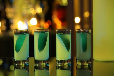 Photo of Shot glasses with alcohol drink and lime wedges on mirror surface against blurred background