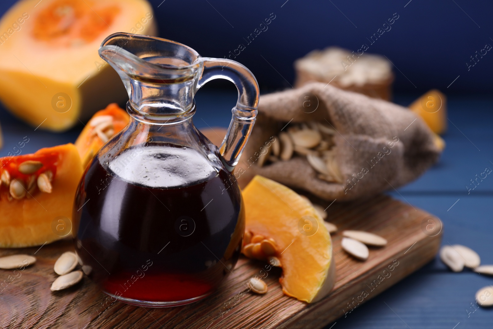 Photo of Fresh pumpkin seed oil in glass jug on blue wooden table