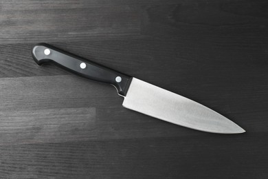 Photo of One sharp knife on black wooden table, top view