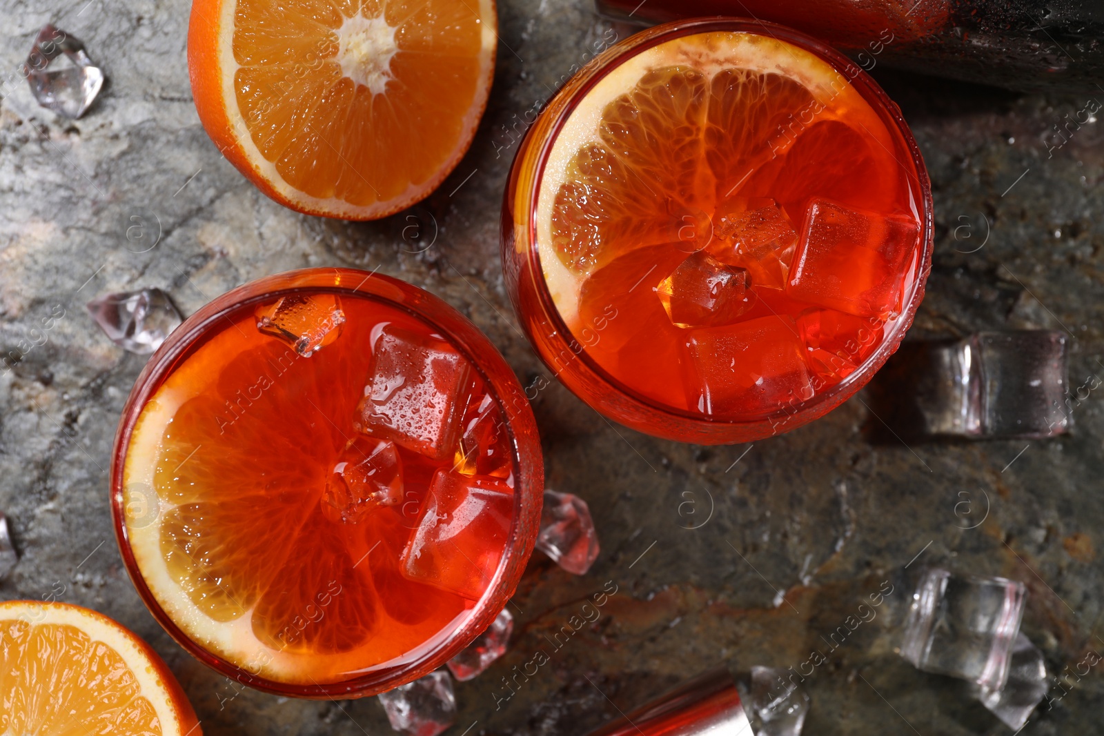 Photo of Aperol spritz cocktail, ice cubes and orange slices in glasses on grey textured table, top view