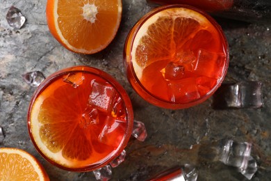 Photo of Aperol spritz cocktail, ice cubes and orange slices in glasses on grey textured table, top view