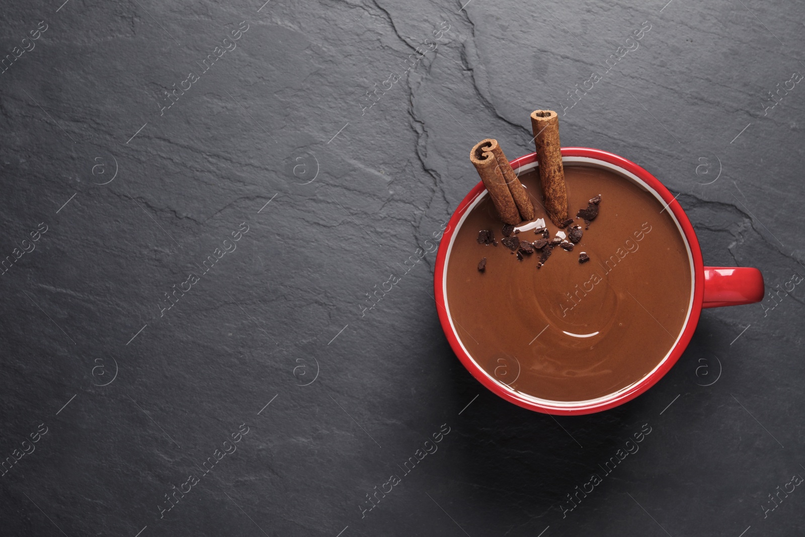 Photo of Yummy hot chocolate with cinnamon in red cup on black table, top view. Space for text