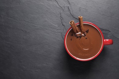 Photo of Yummy hot chocolate with cinnamon in red cup on black table, top view. Space for text